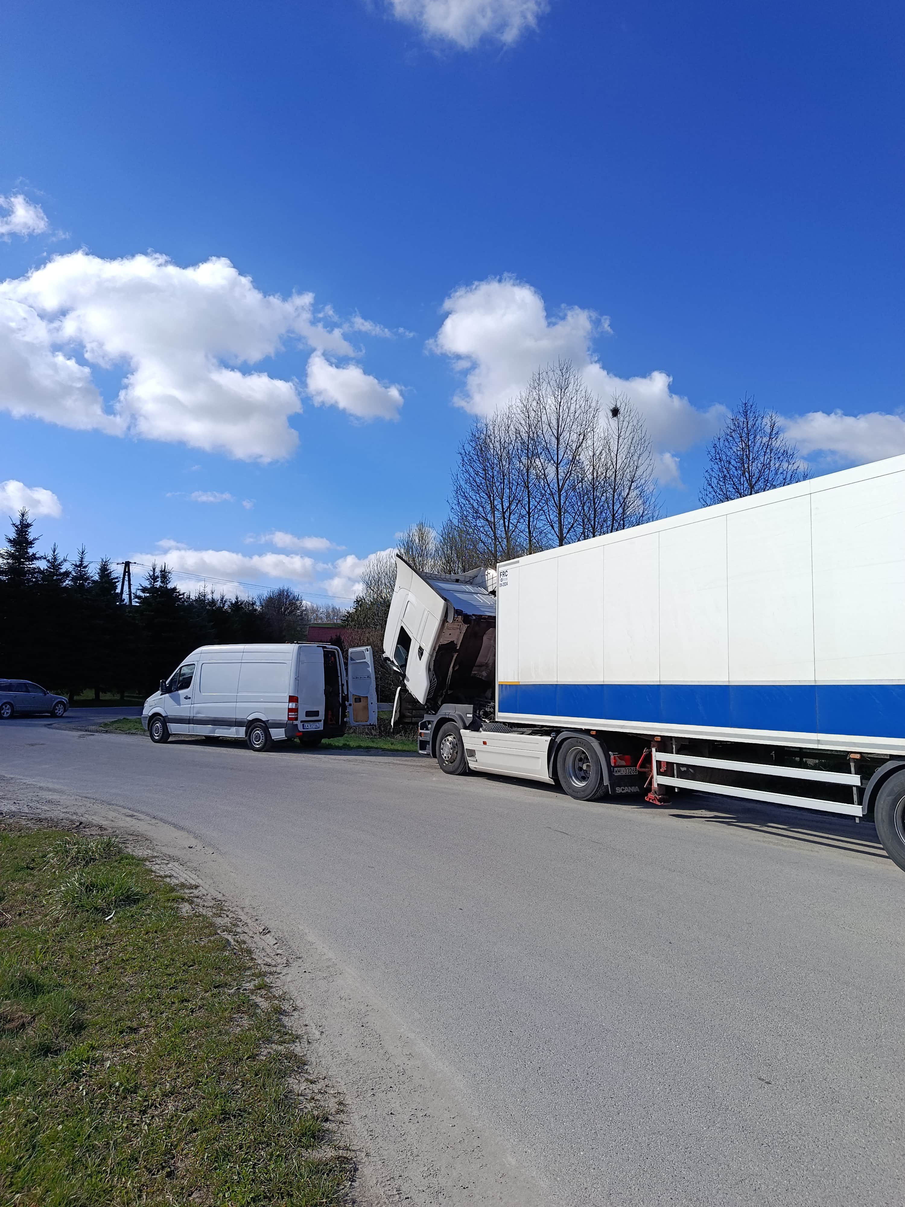 Nocna naprawa ciągnika siodłowego przez mobilny serwis TIR, otwarty bus warsztatowy i podniesiona kabina ciężarówki na ulicy