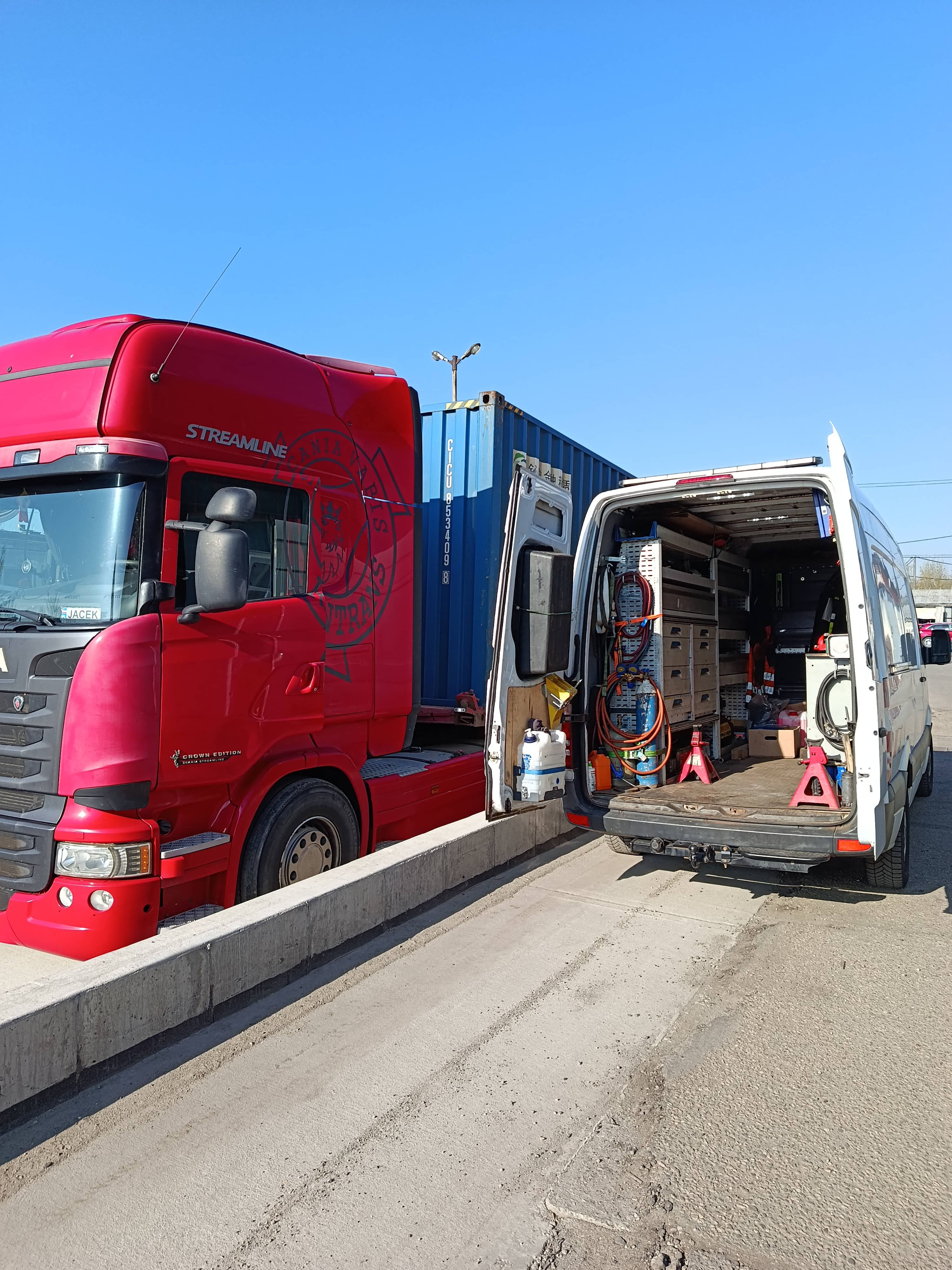 Nocna awaria naczepy ciężarowej, mobilny mechanik TIR naprawiający oś przy sztucznym oświetleniu z busa serwisowego