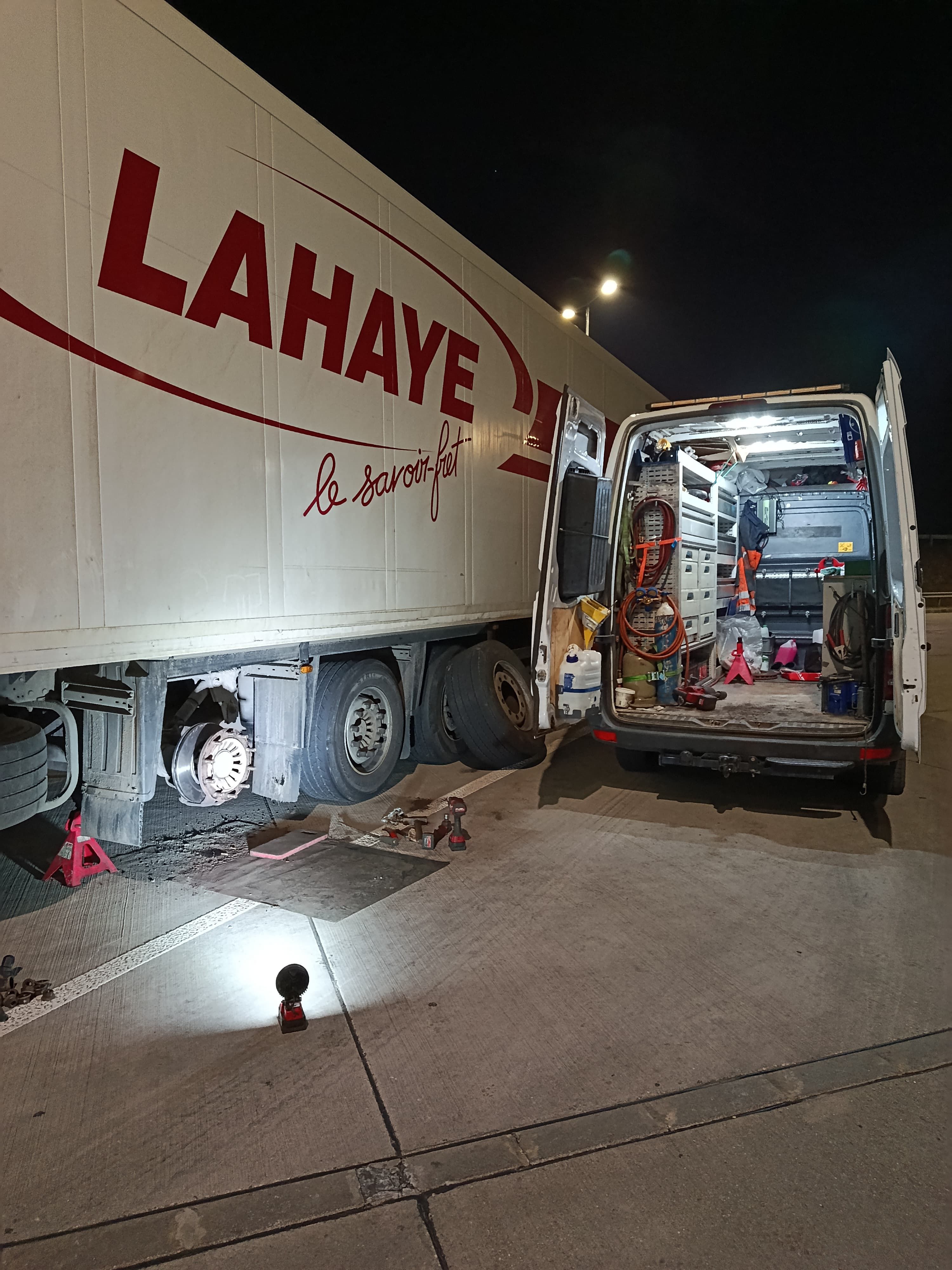 Mechanik mobilnego serwisu TIR podczas wymiany sprzęgła w ciężarówce, widoczny specjalistyczny dźwig i komora silnika