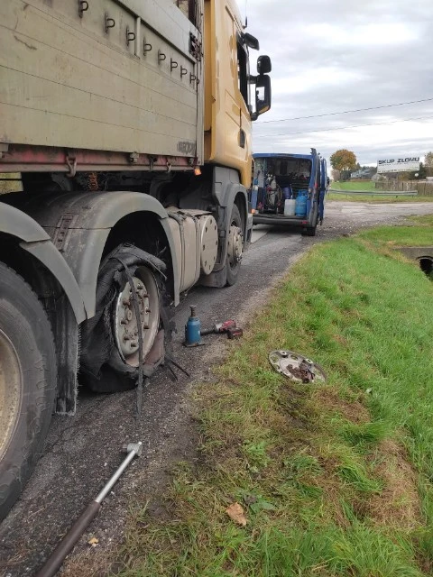 Wymiana koła ciężarówki na poboczu drogi, narzędzia i zepsuty piasta koła na ziemi.